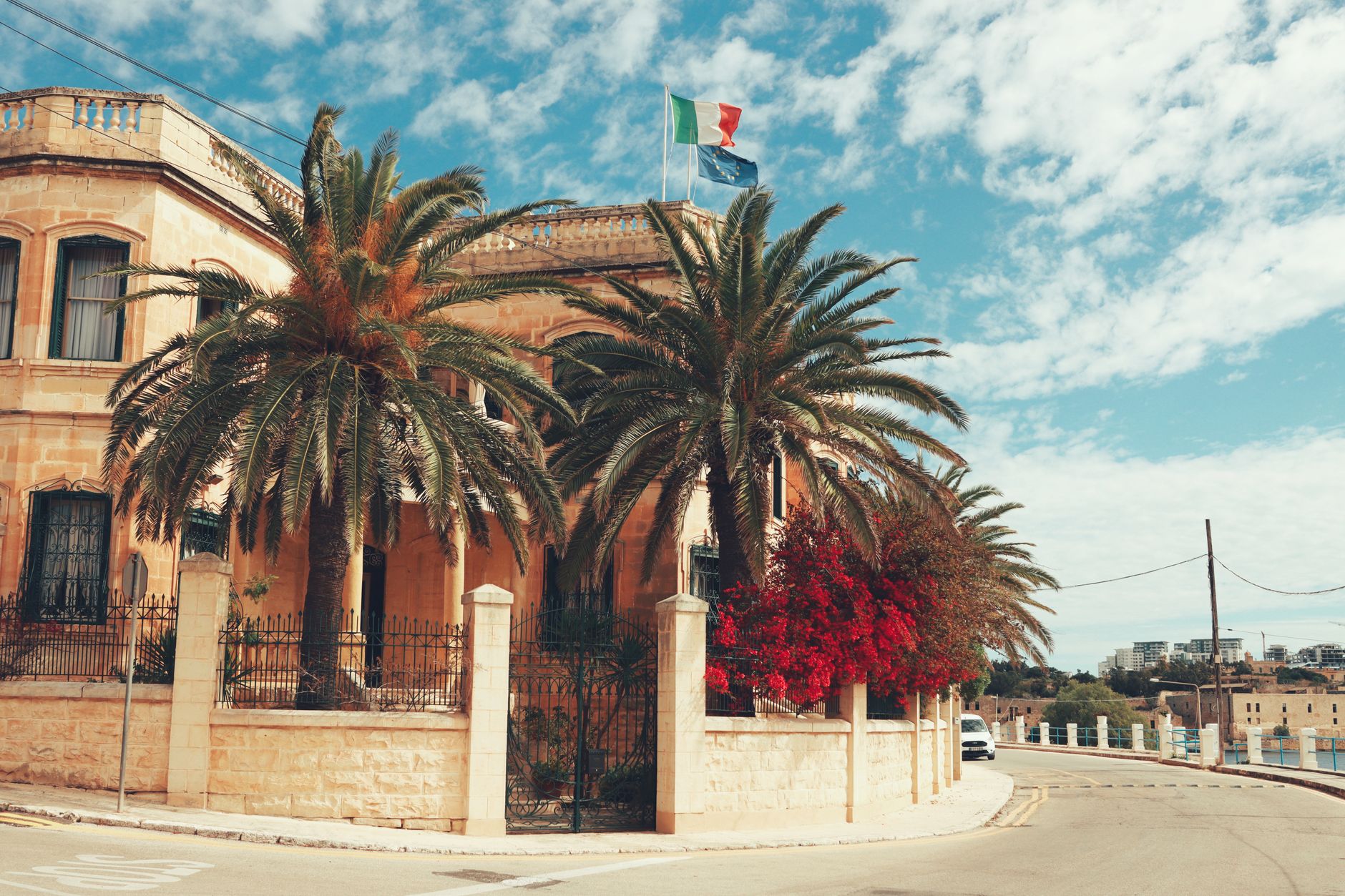 Elegant villa surrounded by palm trees in Valletta, showcasing classic Maltese architecture with a vibrant sky